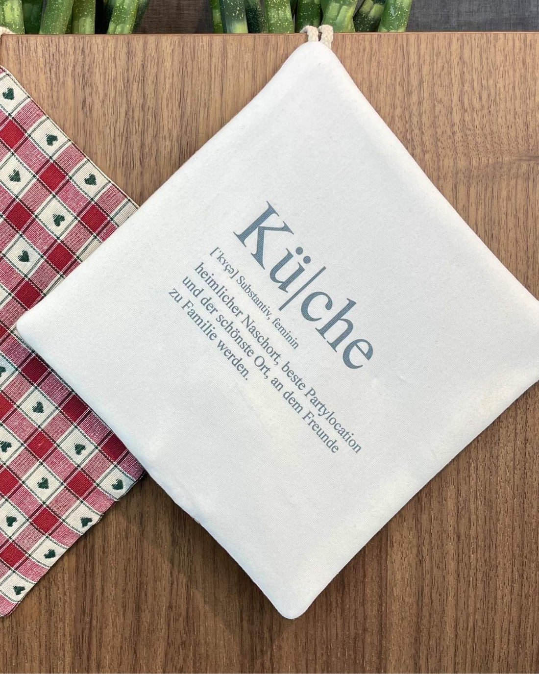 Topflappen mit Definition „Küche“ als Aufdruck neben rot-grünem Herzmuster
