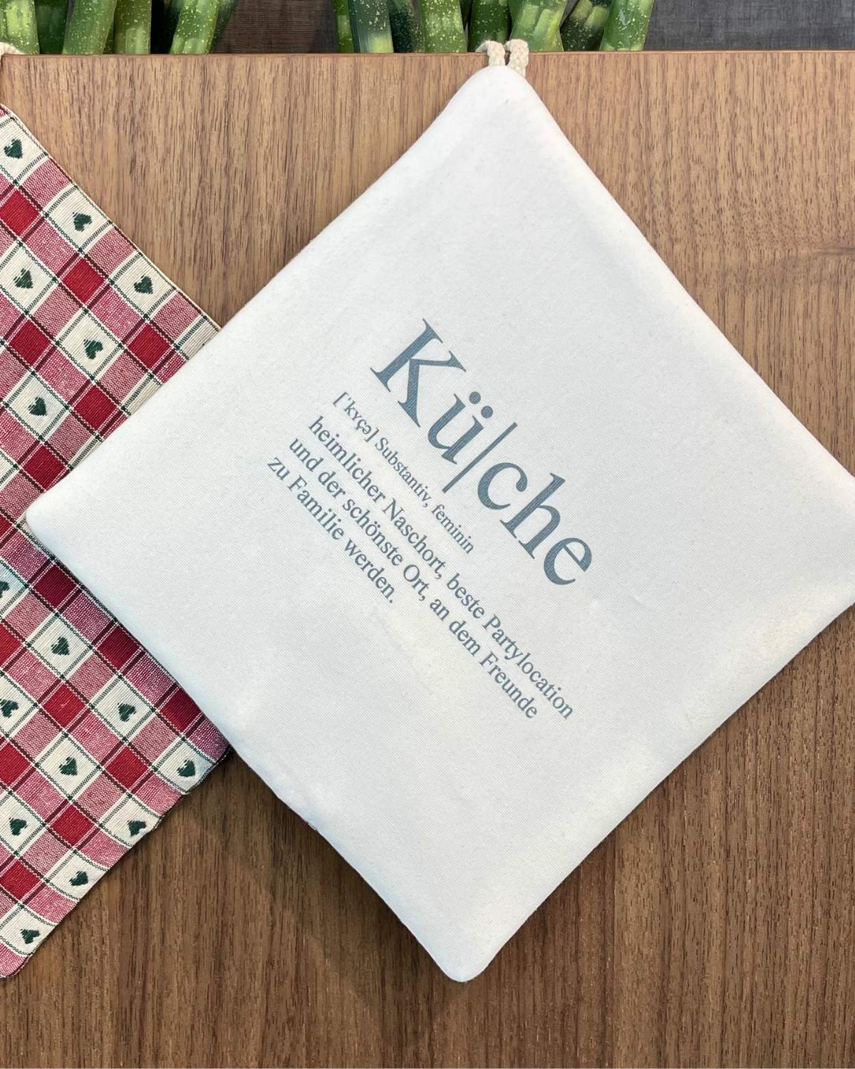 Topflappen mit Definition „Küche“ als Aufdruck neben rot-grünem Herzmuster